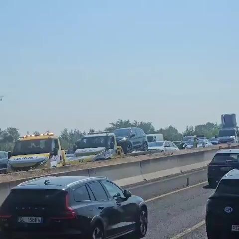The video shows a traffic jam on a highway. Several cars and tow trucks are visible, suggesting an accident or breakdown. The sky is clear and blue, and trees are visible in the background. The traffic appears to be at a standstill, with cars lined up on the highway. One tow truck is in the process of loading a damaged vehicle. The scene is consistent with a highway incident that has caused significant delays.