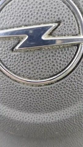 A close-up video reveals an Opel car's steering wheel with the brand's logo prominently displayed. A hand enters the frame holding a Marshall from Paw Patrol plushie in front of the steering wheel. The plushie is white with black spots, wearing a red firefighter uniform and hat.
