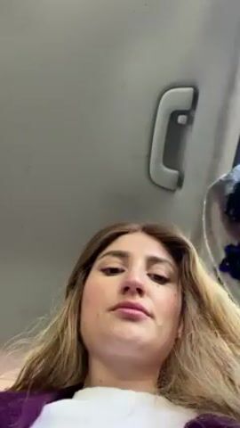 A woman in a car puts on a gray headband. The headband has a dark blue design on the side and in the center. The car’s ceiling and handle are visible in the background. The woman looks at the camera after putting on the headband. She is wearing a purple top. The video is shot from a low angle.