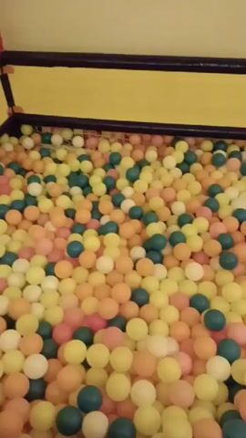 THE VIDEO SHOWS A BALL PIT FILLED WITH MANY SMALL, ROUND BALLS OF VARIOUS COLORS INCLUDING YELLOW, ORANGE, PINK, AND BLUE. THE BALL PIT APPEARS TO BE INDOORS WITH YELLOW WALLS AND A DARK COLORED EDGE. THE CAMERA MOVES SLIGHTLY, PROVIDING A CLOSE-UP VIEW OF THE BALLS, AND OCCASIONALLY SHOWS A SLIGHT GLIMPSE OF THE WALLS AND EDGES OF THE BALL PIT.