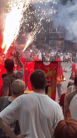 Street parade with red costumes, flares, and a dragon float
