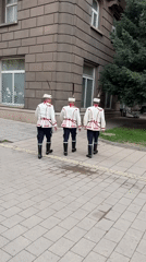 Three men in traditional ceremonial uniforms walk in Sofia