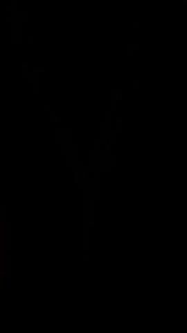This is a short video with a dark background. The subject is a sparkly, multi-strand necklace that hangs in a V-shape. The necklace appears to be made of small, shimmering beads. The lighting is low, making the necklace stand out against the darkness. There are a few faint, out-of-focus lights visible in the background in the first few frames, but they disappear as the video progresses. No people are visible. The overall mood is mysterious and elegant. There is no visible text in the video.