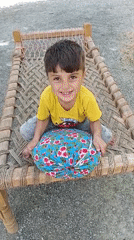 Child plays on traditional bed in Pakistani village courtyard