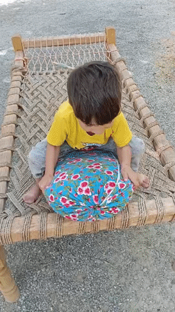 Child plays on traditional bed in Pakistani village courtyard