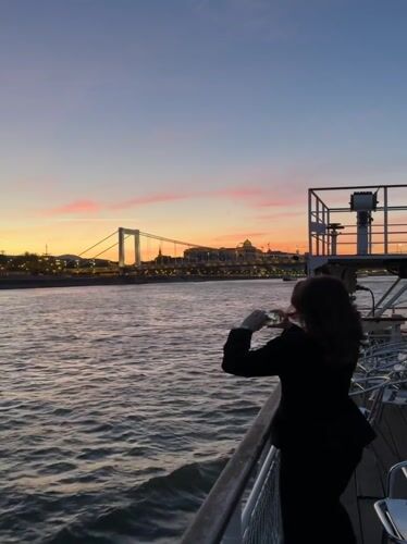Woman photographs Budapest sunset from Danube River boat cruise