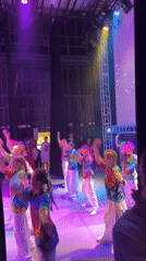 Children perform synchronized dance in tie-dye shirts on stage
