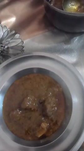 The video shows a table with several dishes on it. At the start, a person uses a ladle to scoop some liquid from a dark pot. The camera moves to another plate with a portion of white rice and a portion of brown liquid. Next, the camera focuses on a plate of brown liquid, seemingly gravy or sauce. The camera moves again, and there are two metal plates visible, one with brown liquid and the other partially visible. The camera seems to be held by someone who is moving or filming quickly, causing blurriness. The scene seems to depict someone serving or preparing food.