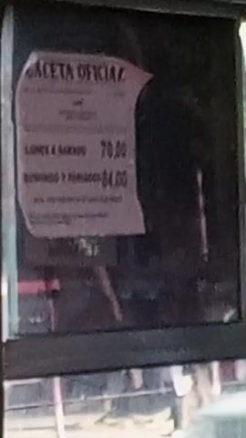 The video shows the interior of a bus in transit, evidenced by the presence of seated passengers and a posted fare sign indicating different rates for weekdays/Saturdays (70.00) and Sundays/holidays (84.00). The video then focuses on a hand holding what appear to be three folded banknotes. The bus interior features red seats and a white ceiling with overhead lighting.