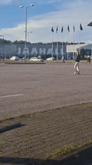 Dirt bike wheelies in a paved lot outside a large building