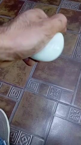 A hand is squeezing two white eggs. The eggs are being squeezed with the thumb and fingers of the right hand. The background is a tiled floor.