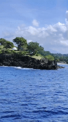 People gather on rocky coastline near tents in Karangasem