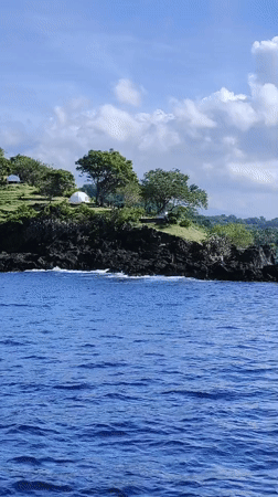 People gather on rocky coastline near tents in Karangasem