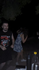 Young adults dance at nighttime outdoor gathering in Greece