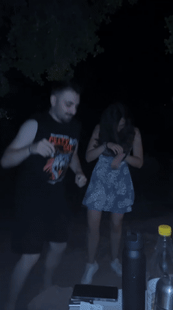Young adults dance at nighttime outdoor gathering in Greece