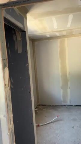 The video captures the interior of an unfinished room, likely part of a building under renovation or construction in South Oxfordshire, United Kingdom, during daytime. The walls and ceiling are covered with drywall, and the seams have been taped and mudded, with some areas appearing to be still wet or drying.

A white-framed window is visible on one wall, providing natural light to the room. The floor is bare concrete, and a white PEX pipe with a red cap or fitting is lying on it. The camera pans from a doorway into the room. On the left side of the doorway frame, the text "BRITISH GYPSUM" is partially discernible. No people are visible in the scene.