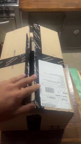 A person receives a cardboard box from an online order. The box is secured with black tape that says, “Gracias por Comprar.” The label on the box includes the word, “PICKIT.” The person then opens the box, which reveals it is for Nike. The box appears to be empty.