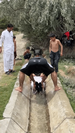 Group cools off in a concrete water channel in rural Pakistan