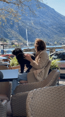 Woman enjoys morning cafe moment with small dog in Kotor Bay