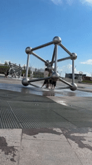 People cool off around a modern sculptural fountain on a sunny day