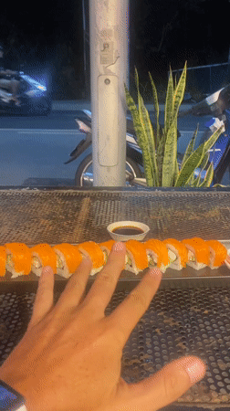Hand reaches for salmon sushi at outdoor Thailand location
