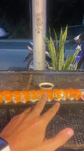 Hand reaches for salmon sushi at outdoor Thailand location