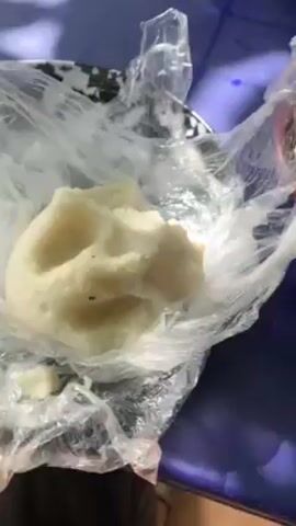 A video shows a plate of mashed potatoes inside a plastic bag. A person takes a piece of the potatoes and dips it into a dark green sauce. Other food items are visible on the table including a bowl of broth and another dish with meat and spices. The table is blue.