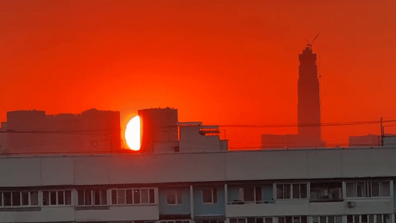 City skyline glows under a deep orange and red sunset.