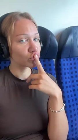 A blonde woman with headphones on is sitting on a train. In the first clip, she has her finger to her lips, appearing to be shushing. In the subsequent clips, she rests her head on her hand, looking bored, and makes a pouting expression. She wears a dark t-shirt and a bracelet. The train seats are blue and patterned. The background shows a blurred green landscape and a bright sky.