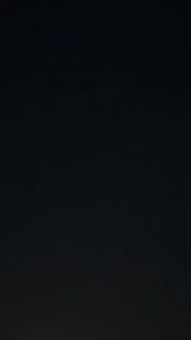 A video clip shows a dark sky with a full moon. The moon is in the center of the frame, and it is very bright. The moon is round and appears to be glowing. The sky is dark and there are no stars visible. There is a faint silhouette of trees at the bottom of the frame.