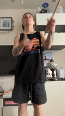 Person juggles drumsticks indoors in Dolgoprudny wearing California-themed clothing