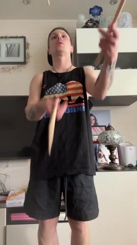 Person juggles drumsticks indoors in Dolgoprudny wearing California-themed clothing