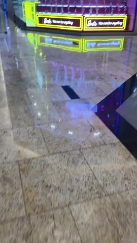 This media file showcases a brightly lit Barbie-themed display in what appears to be a shopping mall or retail space. The display is designed to evoke a sense of fantasy and aspiration, aligning with the brand's message.

**Subjects:**
The primary subjects are dolls, predominantly Barbie dolls, arranged on tiered shelves. At the top of the display, several larger Barbie dolls and some Ken dolls are prominently featured, standing as if in a fashion show or presentation. The dolls represent a variety of styles and ethnicities. The scene also includes reflections on the polished floor, creating a visual echo of the display above.

**Objects and Scene:**
The scene is a retail display, likely a storefront window or an in-store promotional area. The background is a vibrant wall adorned with Barbie branding and thematic elements. Neon signs, stars, palm trees, sunglasses, and roller skates contribute to the playful and whimsical atmosphere. The display itself is structured in a stepped pyramid shape, allowing for maximum visibility of the numerous dolls. The floor is highly reflective, enhancing the visual impact of the bright lights and colors from the display.

**Activity or Event:**
The media file captures a static display, suggesting a product showcase or a brand promotion. There is no active event taking place within the frame, other than the implied activity of shopping or browsing. The display is designed to attract attention and generate interest in Barbie products.

**Notable Details:**
The lighting is bright and artificial, suggesting it could be daytime or evening in an indoor, climate-controlled environment. The reflective floor indicates a clean and modern setting, characteristic of many shopping malls. The overall emotion conveyed is one of joy, fantasy, and aspirational play, core to the Barbie brand. The location context mentions the United Arab Emirates, which, when combined with the elaborate and often international nature of such displays, suggests a prominent retail hub.

**Visible Text:**
The most prominent visible text reads:
- "Barbie" (repeatedly)
- "dream days"
- "You can be anything" (repeatedly, on neon signs)
- Partial text on the left side of the display, partially obscured, but appears to be "BUILT" or similar, possibly part of an advertisement or brand name.