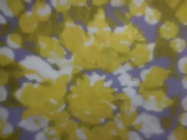 The video shows a close-up of a fabric with a circular pattern. The pattern is made up of yellow and purple floral shapes. The fabric appears to be textured and the image is slightly blurred. The camera is stationary and focuses on the central part of the fabric.