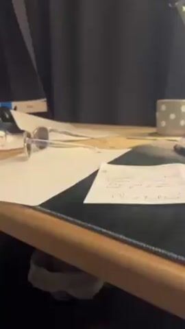 The video shows a desk with various objects on it. There is a pair of O'Neill sunglasses lying on top of some papers. A mug with white polka dots is also visible. A black pen lies on top of another set of papers. A keyboard and desk lamp are partially visible in the background. The desk is made of light wood. The background also includes dark curtains.