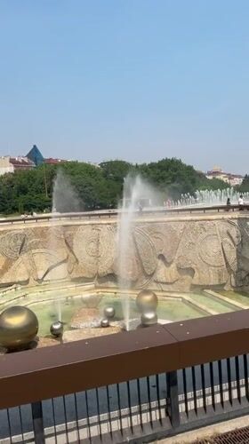 Sunny morning in central Sofia: fountain, flags, and glass facade
