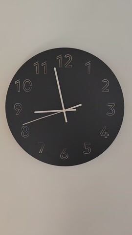The video shows a close-up view of a black wall clock with grey numbers and white hands. The clock is on a light beige or white wall. The time shown is approximately 8:58. The camera is static and the clock is centered in the frame.
