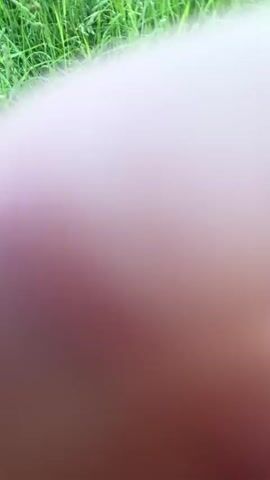 The video shows a first-person perspective of someone walking through tall green grass. The camera is held low, close to the ground, and the grass is so tall that it obscures most of the view. The person's hand occasionally enters the frame, brushing against the grass. The lighting suggests it is daytime, likely outdoors in a natural environment. The sound of rustling grass is audible.