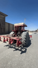 Red tractor with plow heads down a paved road near Quetta