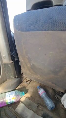The video shows the inside of a vehicle, possibly a van or truck. The interior appears to be stripped down, with exposed metal panels and the absence of typical interior features. There are two plastic water bottles on the floor near the front seats. The back area is empty except for a jacket on the floor and some tools. The doors are open, with only the bare metal frame and windows visible. The overall impression is that the vehicle is either undergoing restoration or is being used for transport purposes with minimal interior fittings.