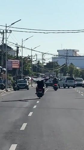 Motorcyclist carries large fabric through North Kuta intersection