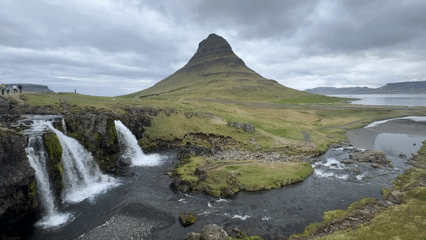 Tourists document Kirkjufell mountain and waterfall under cloudy skies