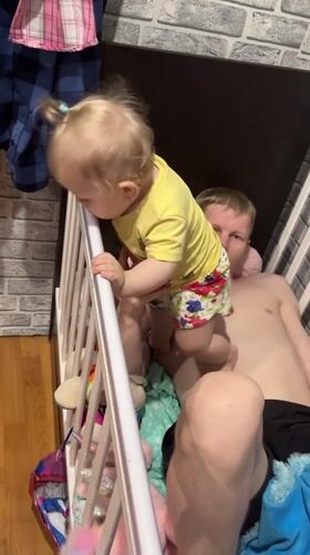 Father and toddler play together inside crib in Russia