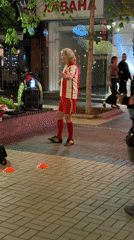 Soccer player in uniform balances object on brick sidewalk