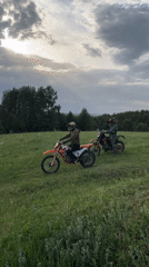 Dirt bike riders navigate grassy terrain, one motorcycle falls