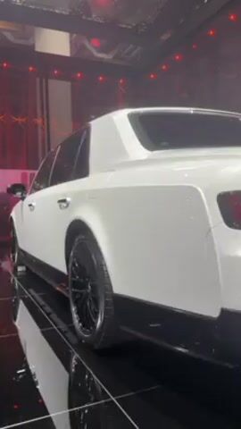 The video shows the rear end of a white Toyota Century, a luxury sedan. The car is parked on a reflective black floor. Red lights adorn the background, giving a stage-like atmosphere. The car has black rims and a black lower trim. The word "CENTURY" is spelled out across the rear, above the tail lights and below the rear window. There is a stylized emblem in the center and "CENTURY" is again on the license plate.