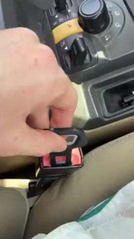 Here's a description of the video:

The video shows the interior of a car, specifically focusing on the center console and the driver's side seat. A hand unbuckles a red seatbelt. The center console features several controls, including levers, a knob, and a series of icons that suggest off-road driving capabilities. The interior appears to be tan or beige in color. The video's lighting is natural, indicating it was likely filmed during the day.