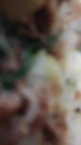 The video is a close-up, blurry shot of food on a piece of paper, with a spoon in the food. The food appears to be a mix of vegetables and possibly meat, with a brownish sauce. The lighting is dim, and the focus is on the food. The spoon is silver and looks like it has been used to eat the food. The paper appears to be a food wrapper or lining. The overall impression is that of a casual meal.