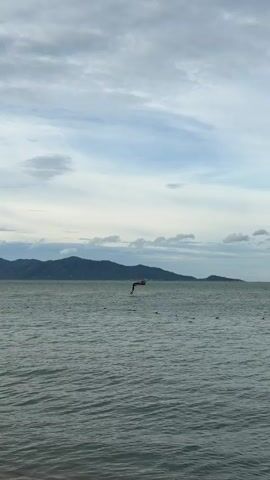 A person is wing foiling on the water. The person is standing on a board with a wing attached to it. The wing is inflated and appears to be made of fabric. The person is holding onto the wing and is using it to propel themselves across the water. The water is choppy and there are waves. In the background, there are mountains and a cloudy sky.