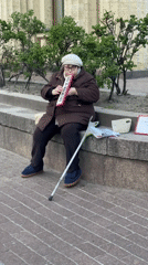 Elderly woman plays melodica on street ledge in Saint Petersburg